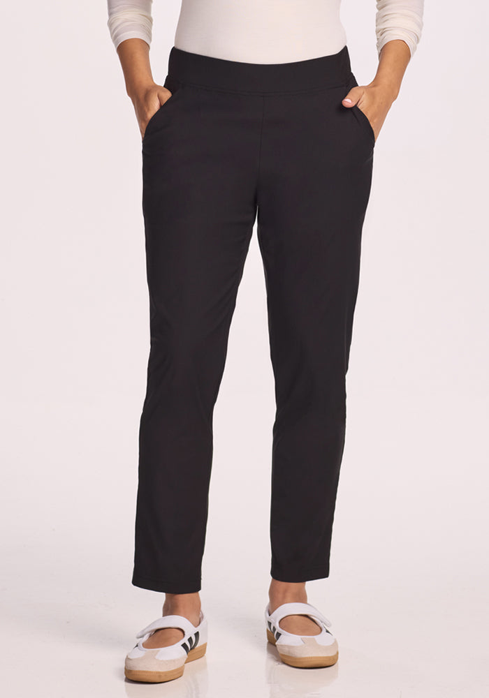 Wearing Woolx Nicole Pants in black, a white long-sleeve top, and white sneakers with beige soles, a person stands with hands in pockets against a plain white background.