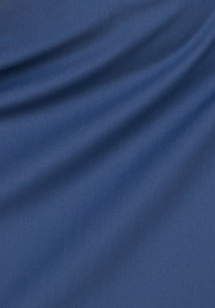 A close-up of the Woolx Nicole Ankle Pants in Vintage Indigo shows blue fabric with diagonal folds and soft shadows, giving a smooth yet textured look typical of these lightweight, breathable pants.