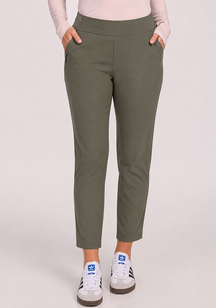 A person wears Woolx Nicole Ankle Pants in Sage Olive, a pale pink top, and white Adidas sneakers with hands in pockets.