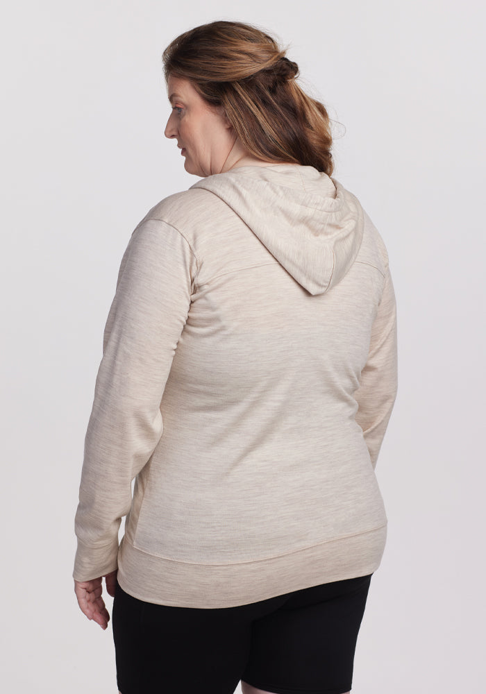 A person with light brown hair shows off the Woolx Ryann Hoodie in Cream Heather from behind, paired with black shorts. Set against a plain white background, the cozy moisture-wicking outfit stands out.