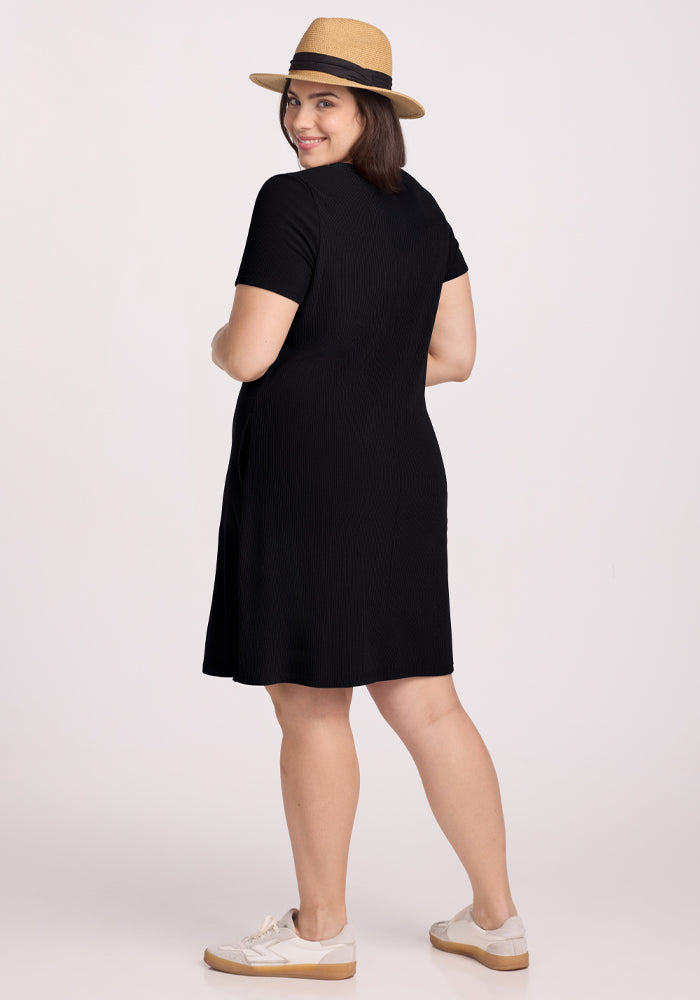 A woman in a Woolx Harlowe Ribbed Dress - Black and a straw hat smiles over her shoulder, wearing white sneakers against a plain white background.