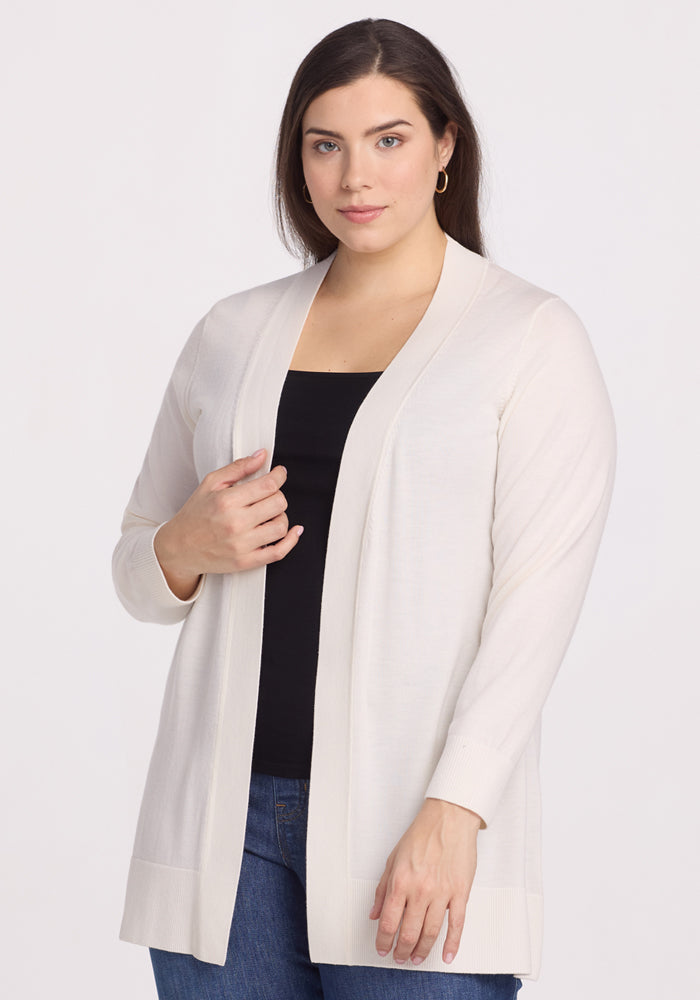 A person with long brown hair is wearing the Woolx Macie Sweater in Dewdrop Pearl over a black top and blue jeans. They have a neutral expression and are standing against a plain white background. 