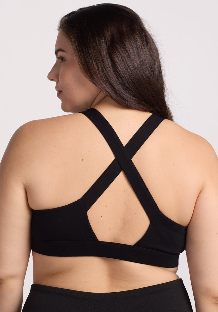 A person with long dark hair is shown from the back wearing the Woolx Livi Bra - Black, a temperature-regulating sports bra with crisscross straps, against a plain white background.