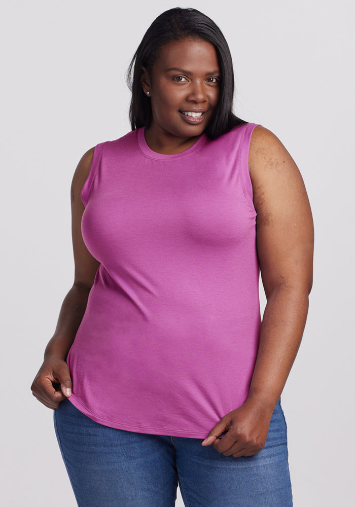 A woman smiles in the Woolx Bella Tunic Top in Purple Wine and blue jeans against a plain light background.