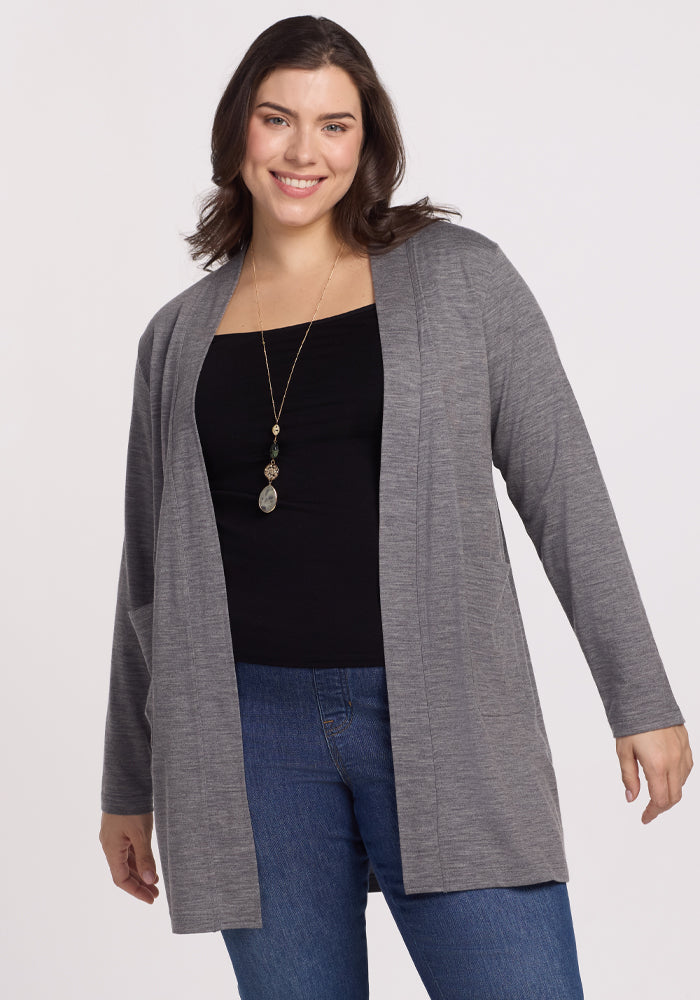 A woman smiles wearing a Woolx Paisley Cardigan in Graphite Heather over a black top and blue jeans. Her long necklace complements her wavy brown hair against the plain white background, exuding effortless style and feather-light comfort. 