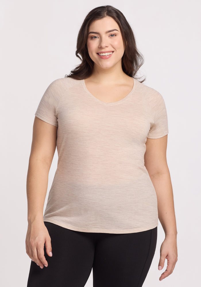 A smiling woman with long dark hair wears the Mia V Neck in Cream Heather by Woolx and black leggings, standing against a plain white background. 