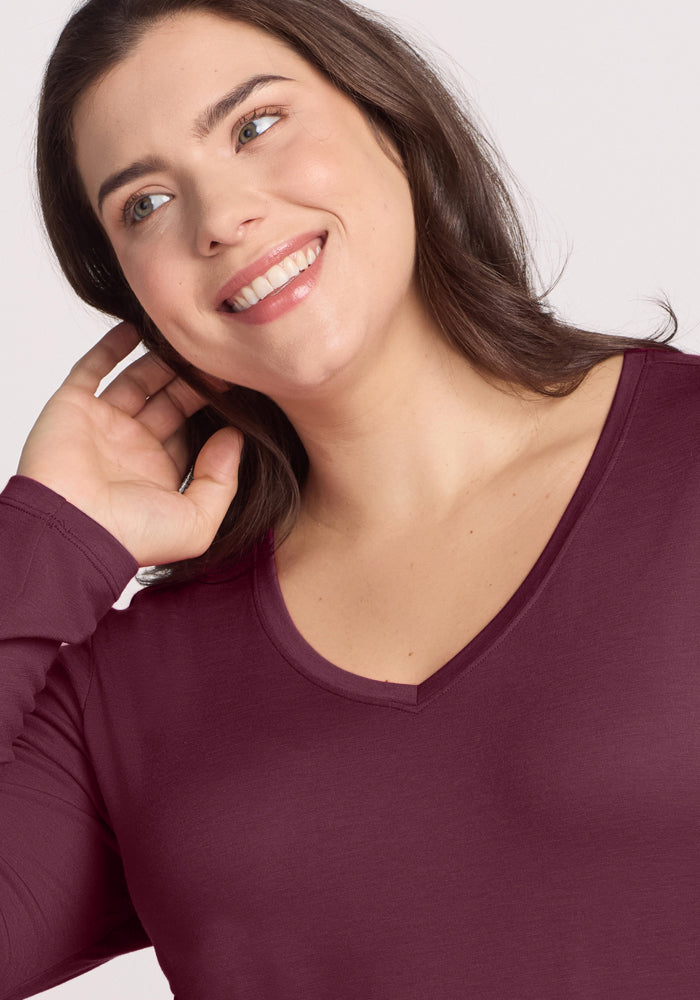Woman with shoulder-length brown hair smiles in the Woolx Millie Long Sleeve in Grape Harvest, touching her hair.