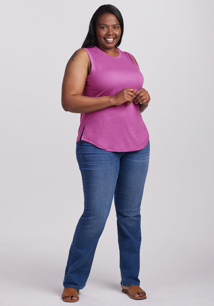Woman in a Woolx Bella Tunic Top in Purple Wine, smiling in blue jeans and sandals against a plain background.