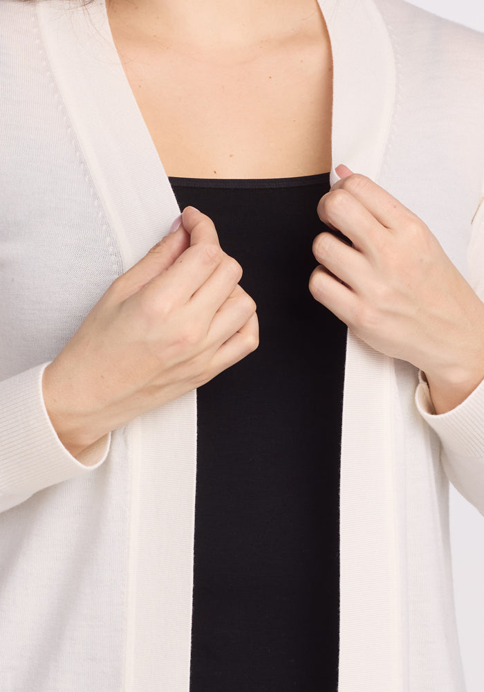 A person is shown adjusting a Woolx Macie Sweater - Dewdrop Pearl over a black top, with the focus on the upper body to highlight the clothing details.