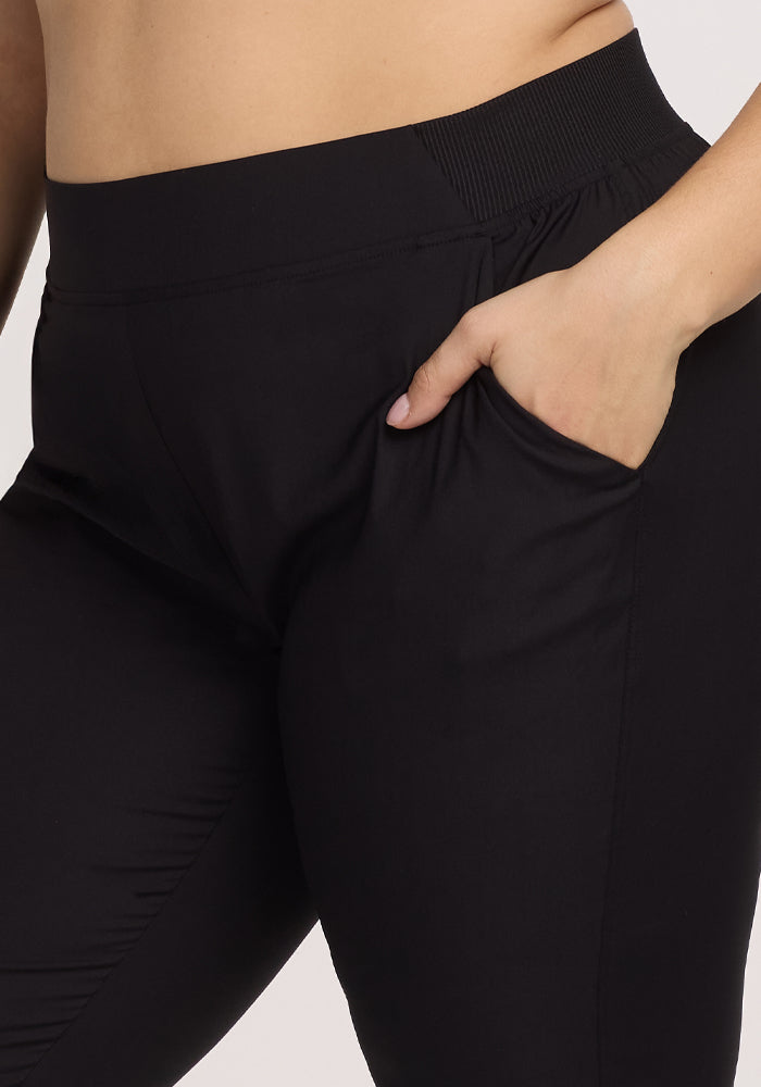 Close-up of a person wearing Woolx Palmer Joggers - Black with one hand in the deep pocket. The image focuses on the waist and hip area, highlighting the joggers' fit and stitching details against a plain white background.