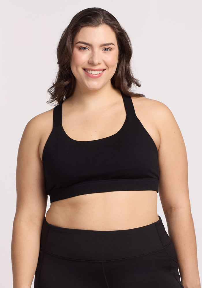 A woman smiles while wearing the Livi Bra - Black by Woolx, featuring double cross-back straps, paired with leggings against a plain white background. 