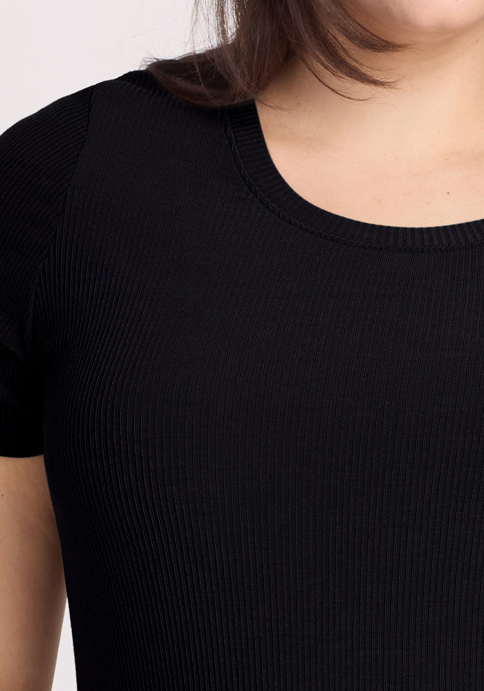 Someone partially visible, from chin to upper arms, is wearing the Woolx Harlowe Ribbed Dress in black against a plain background.