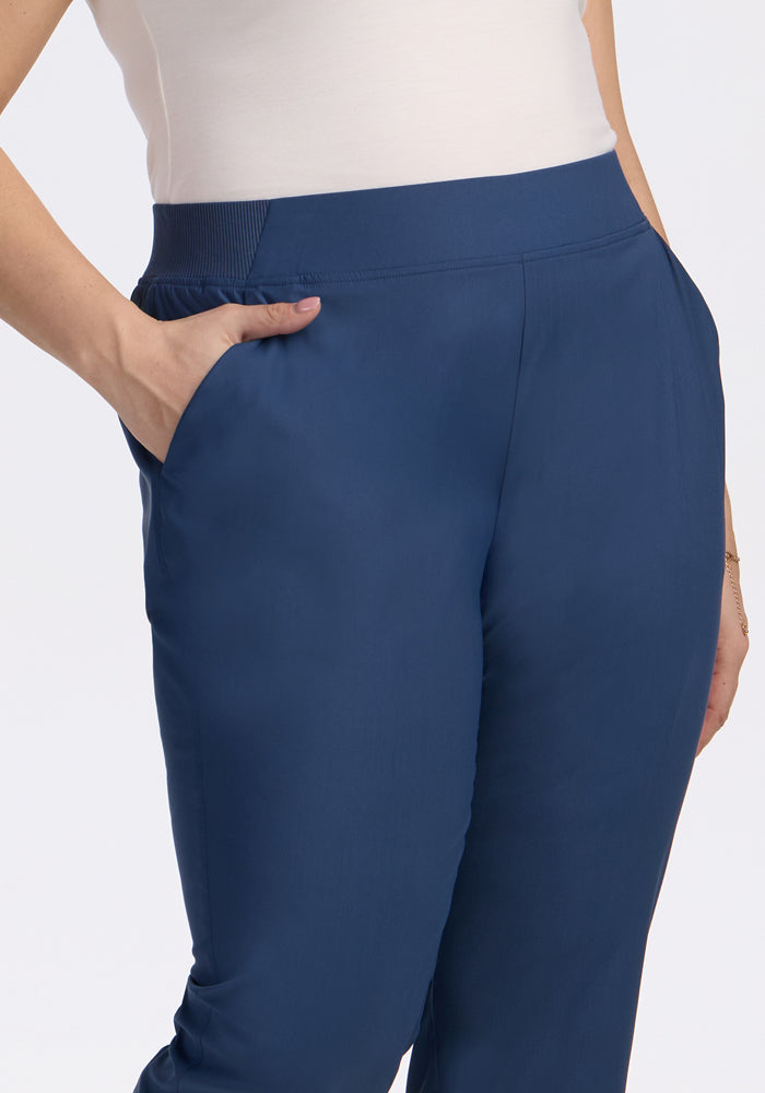 A person wearing a white top and Woolx Palmer Joggers in Vintage Indigo, with their right hand in the pocket, highlighting the waistband, torso, and hip.