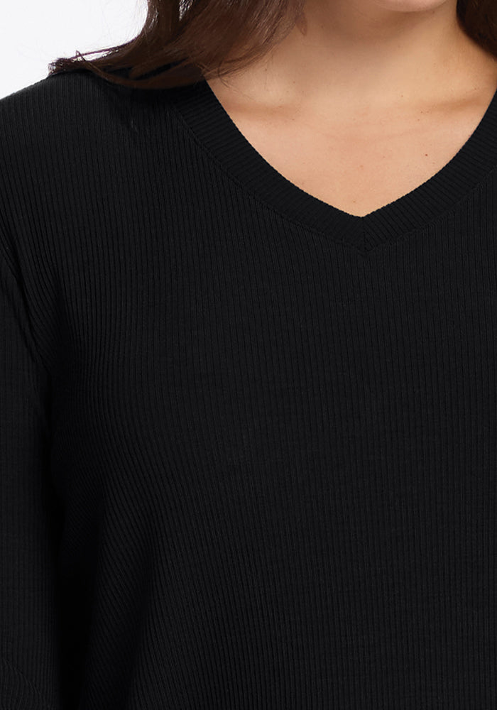 A woman wearing the Woolx Evie Tunic in black, a ribbed Merino wool sweater with a V-neck design. The image emphasizes the upper portion of the tunic, showcasing its cozy texture and flattering fit around the neckline.