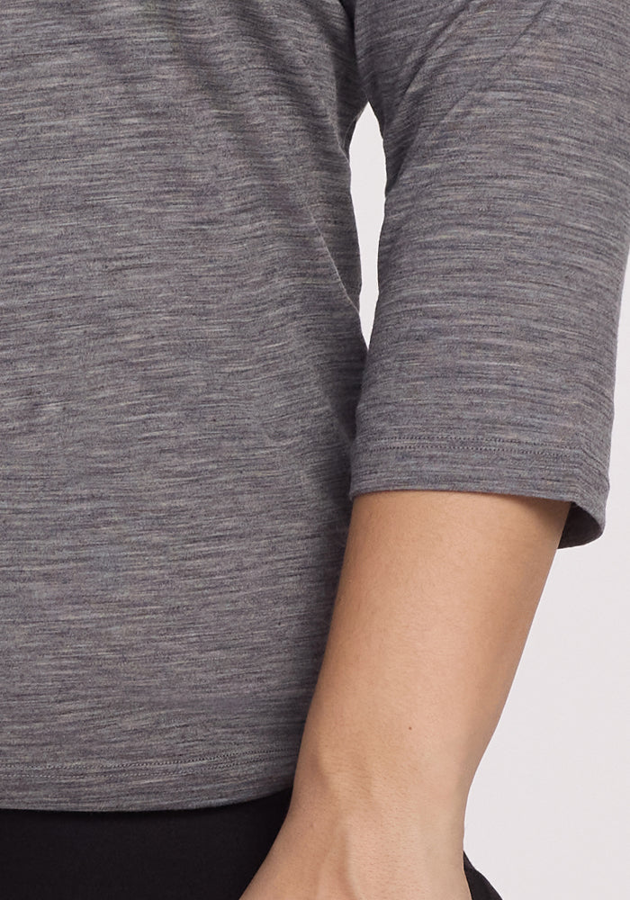 A person is seen wearing the Woolx Elena 3/4 Sleeve V Neck in Graphite Heather. The relaxed fit and bent elbow posture are highlighted beautifully against a plain, light background.