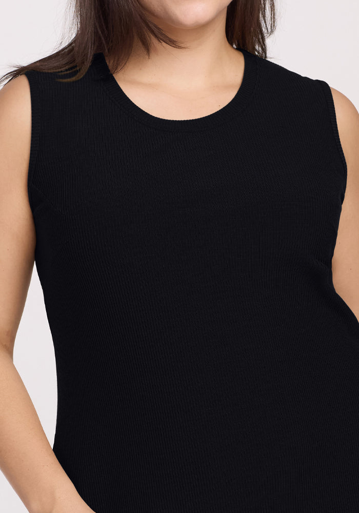 A person wearing the Woolx Iris Ribbed Dress - Black is shown from shoulders to waist, highlighting its texture and fit. The background is plain and light-colored.
