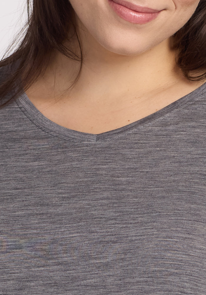 A cropped image highlights the effortless style of a person with long, brown hair wearing a Woolx Elena 3/4 Sleeve V Neck in Graphite Heather. The subtle elegance of their look is complemented by the plain white background.